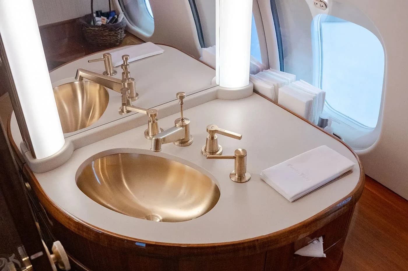 The aircraft lavatory features two gold-colored sinks with matching faucets and a window.