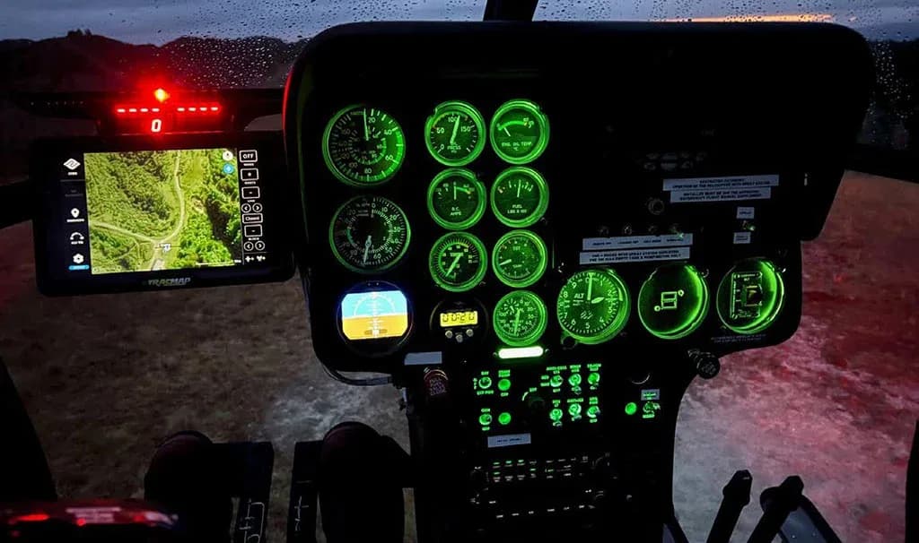 The MD 530 helicopter cockpit instrument panel illuminated with green backlighting at night, showing a GPS display.