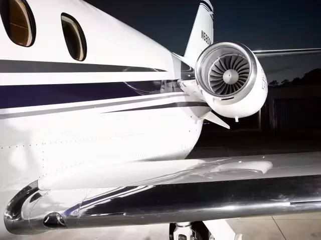 A close-up view of the rear fuselage, engine, and wing of a white business jet with blue and grey stripes.