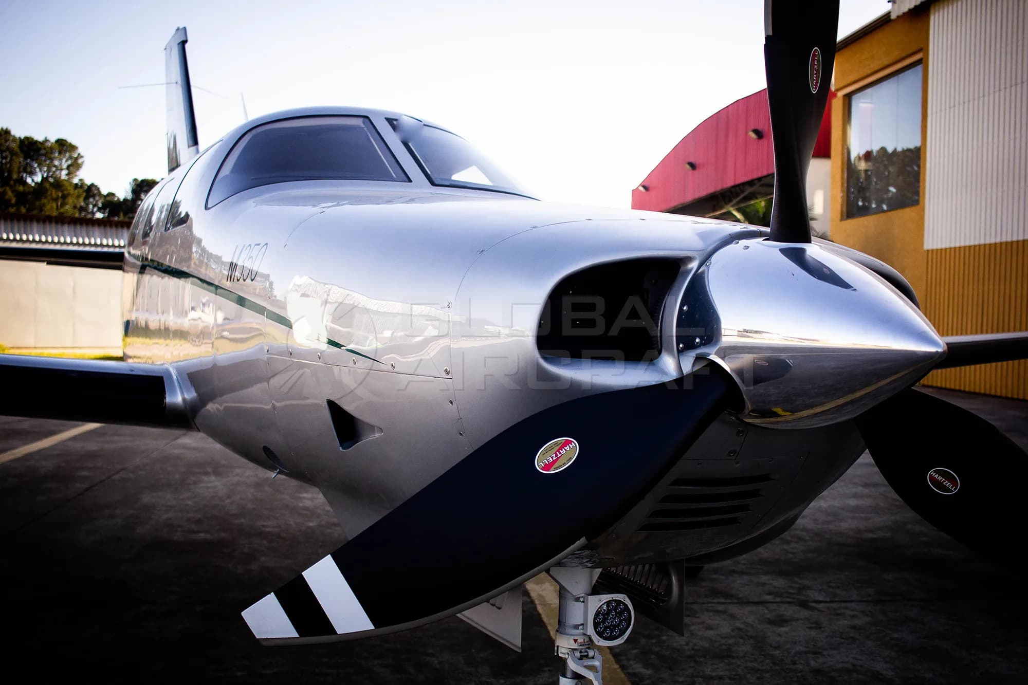 A close-up, low-angle view of the nose and propeller of a silver Piper M350 aircraft.