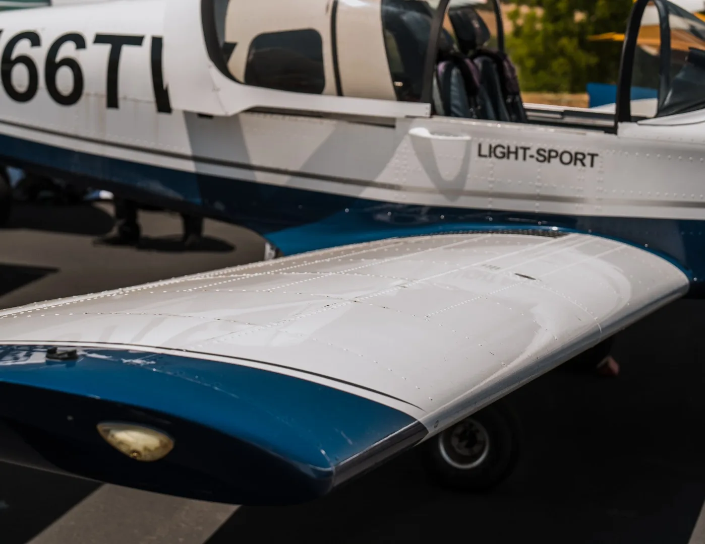 A close-up view of the white wing and blue lower fuselage of the Sling Light-Sport aircraft, N166TW.