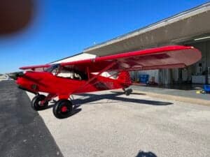 A red aircraft is parked next to a building.