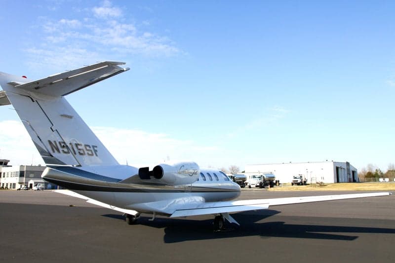 A Citation Jet with tail number N915SF sits on the tarmac in front of a hangar and control tower.