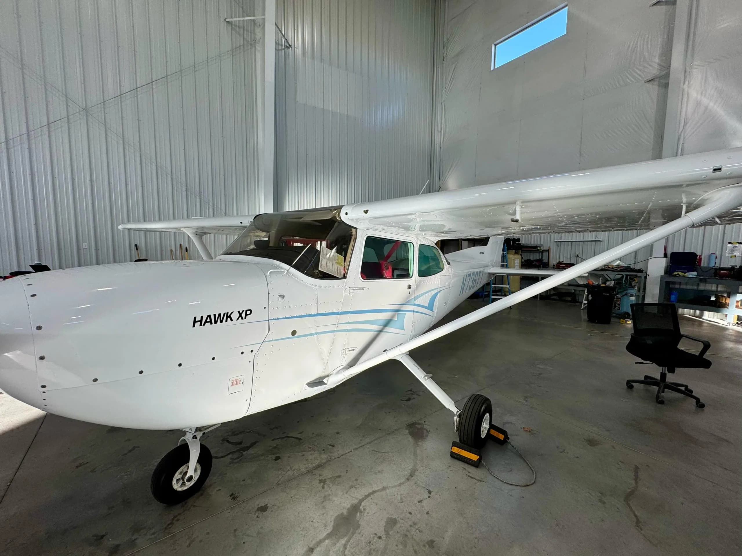 A wide three-quarter front view of a white Cessna 172 Hawk XP aircraft with blue stripes, parked in a hangar.