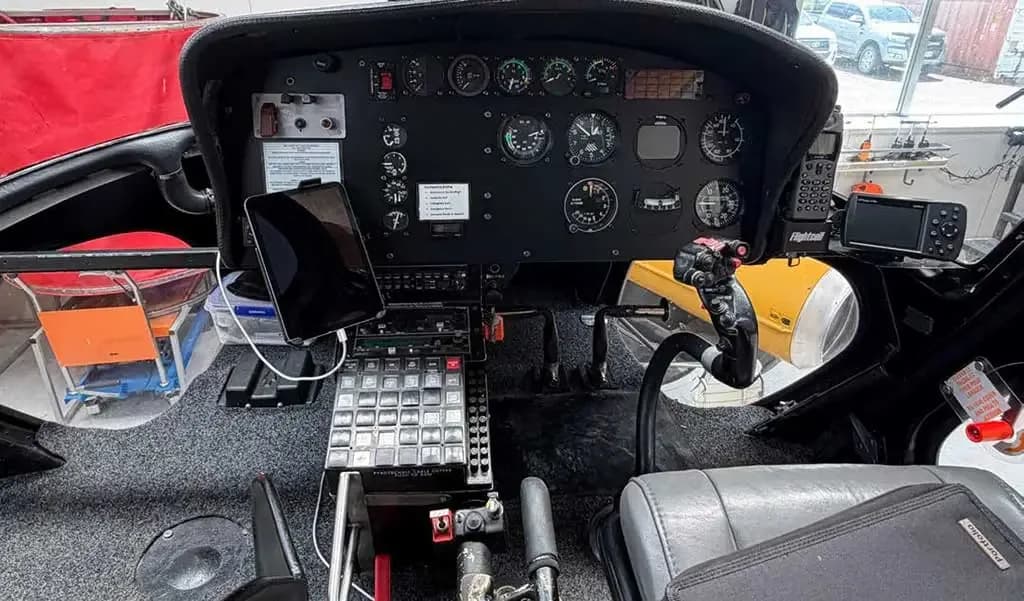 The detailed instrument panel and controls of a helicopter cockpit, with a tablet mounted on the left.