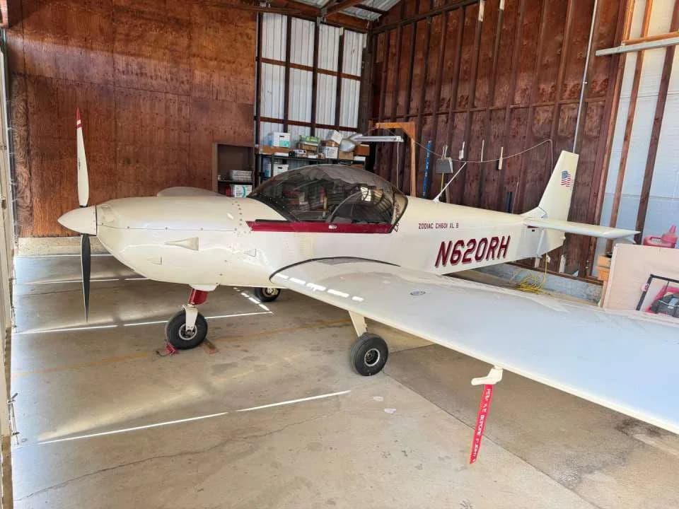 A white Zodiac CH601 XL B aircraft with red trim and registration N620RH parked inside a hangar.