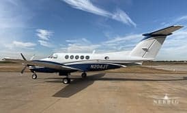 A white and blue twin-engine turboprop aircraft, tail number N204JT, is parked on an asphalt ramp under a partly cloudy sky.