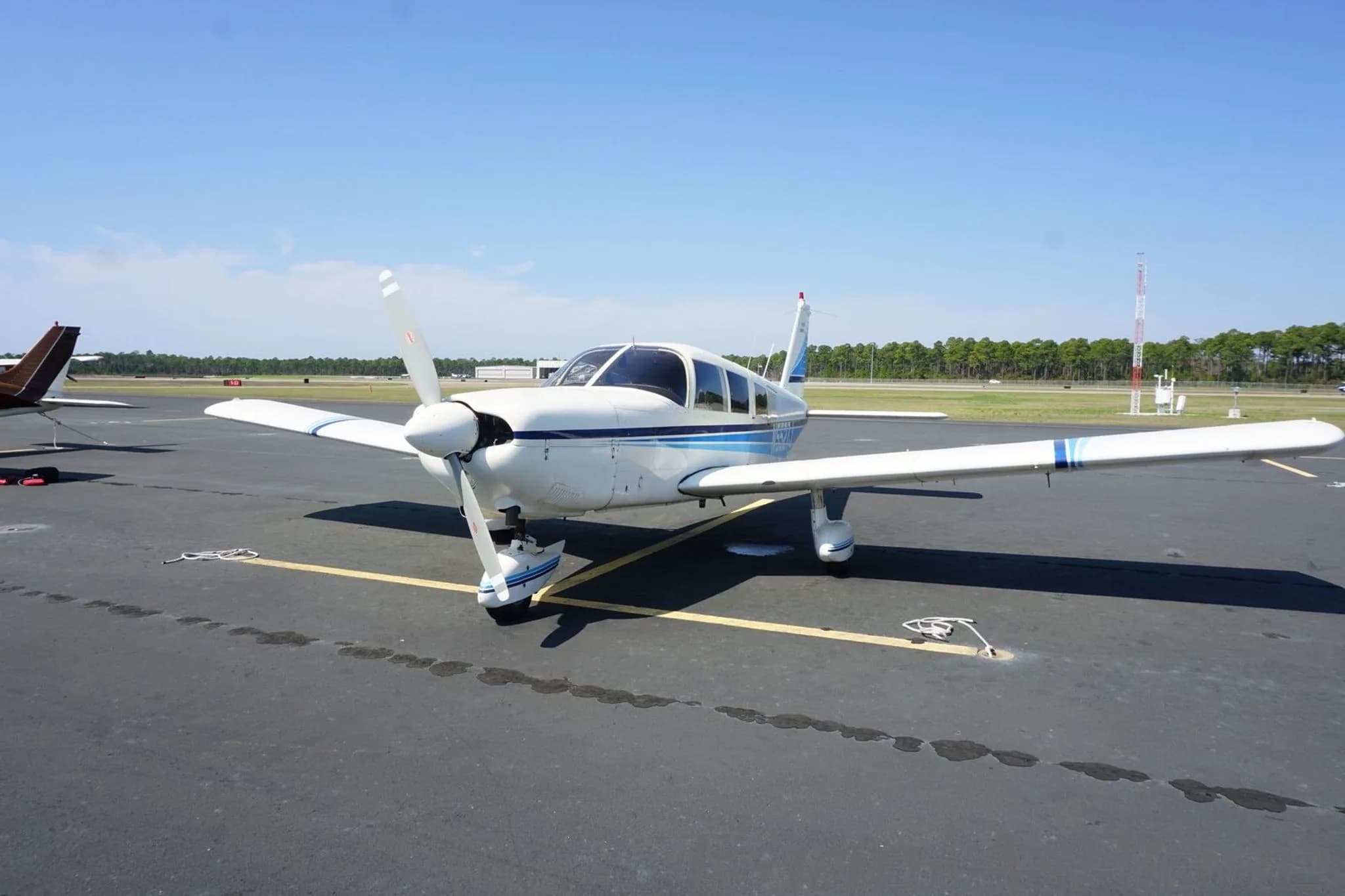 A white single-engine propeller aircraft with blue stripes parked on an airport tarmac.