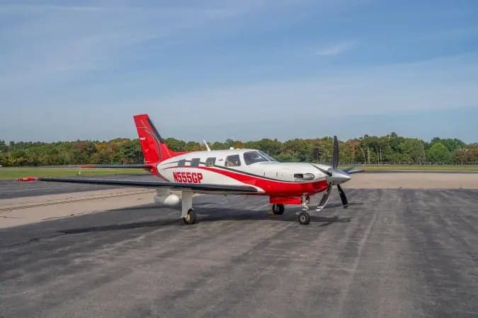 A white and red Piper M-class single-engine turboprop aircraft with registration N555GP parked on an asphalt ramp under a blue sky.