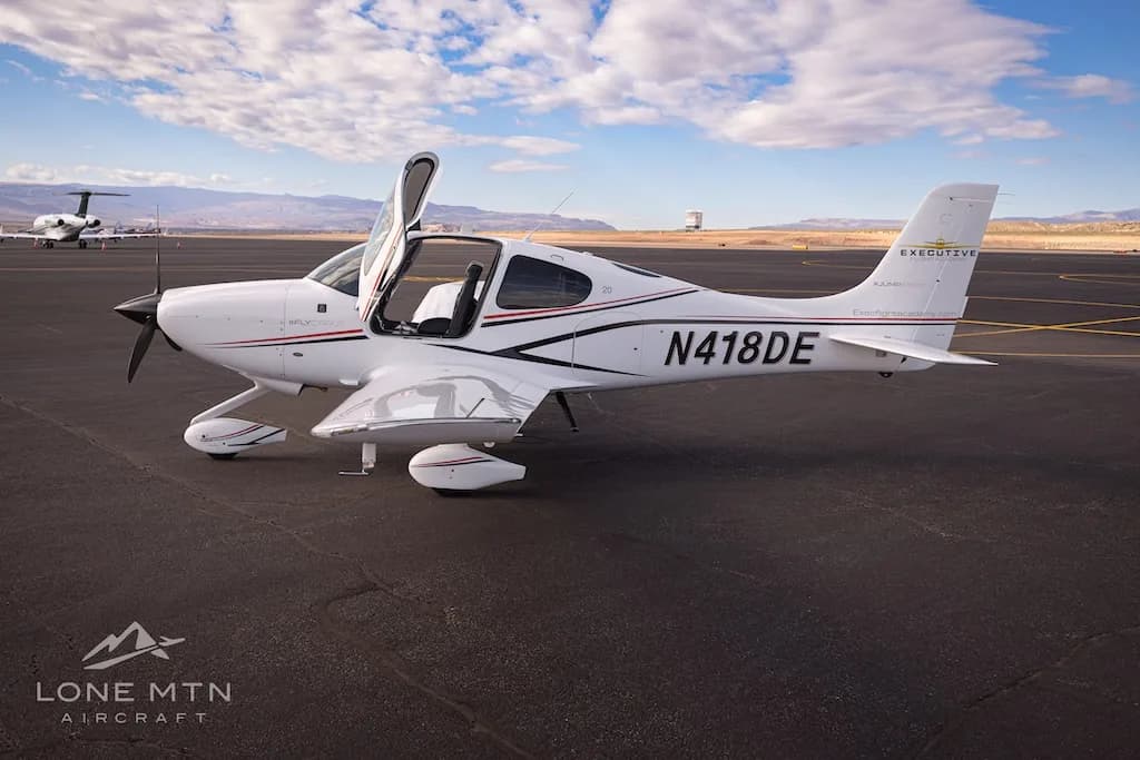 A white Cirrus SR22 aircraft with black and red stripes, registration N418DE, parked on an airfield with doors open.