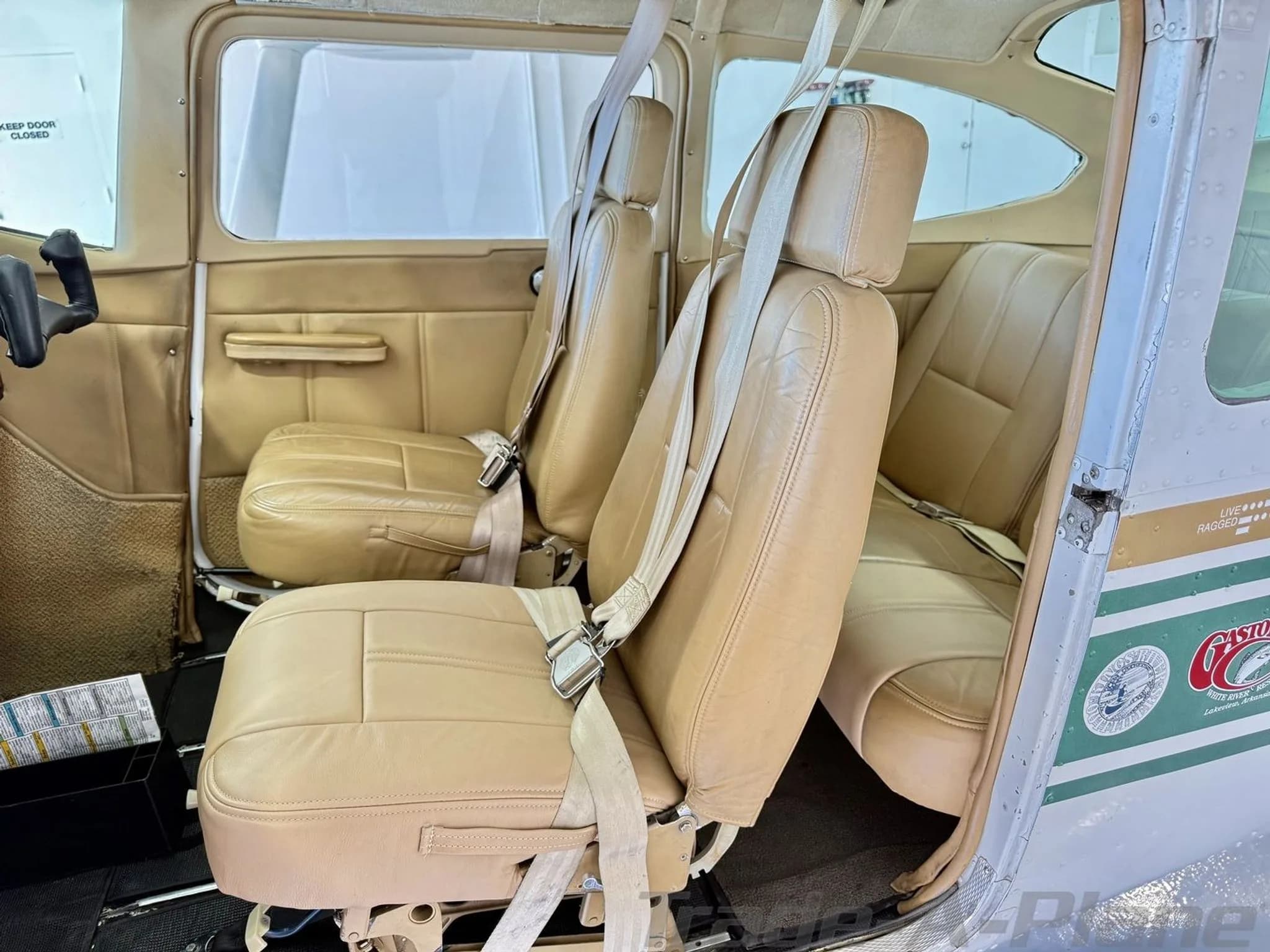 The tan leather interior of the aircraft cabin with two front seats and a rear bench seat.