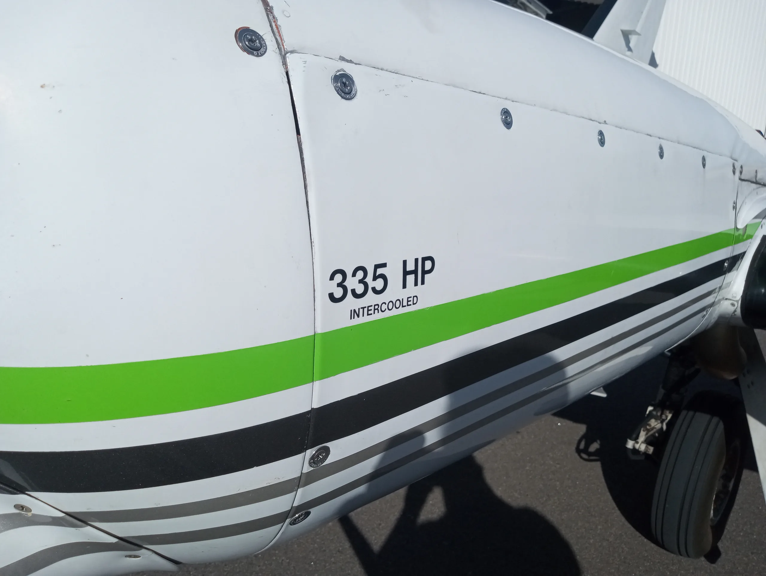 A close-up of the white fuselage of the aircraft, showing "335 HP INTERCOOLED" text and green and black stripes.