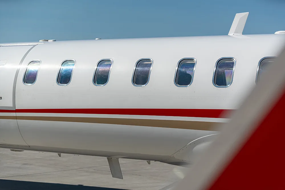 A close-up of the side of a white private jet fuselage with passenger windows and red and gold stripes.