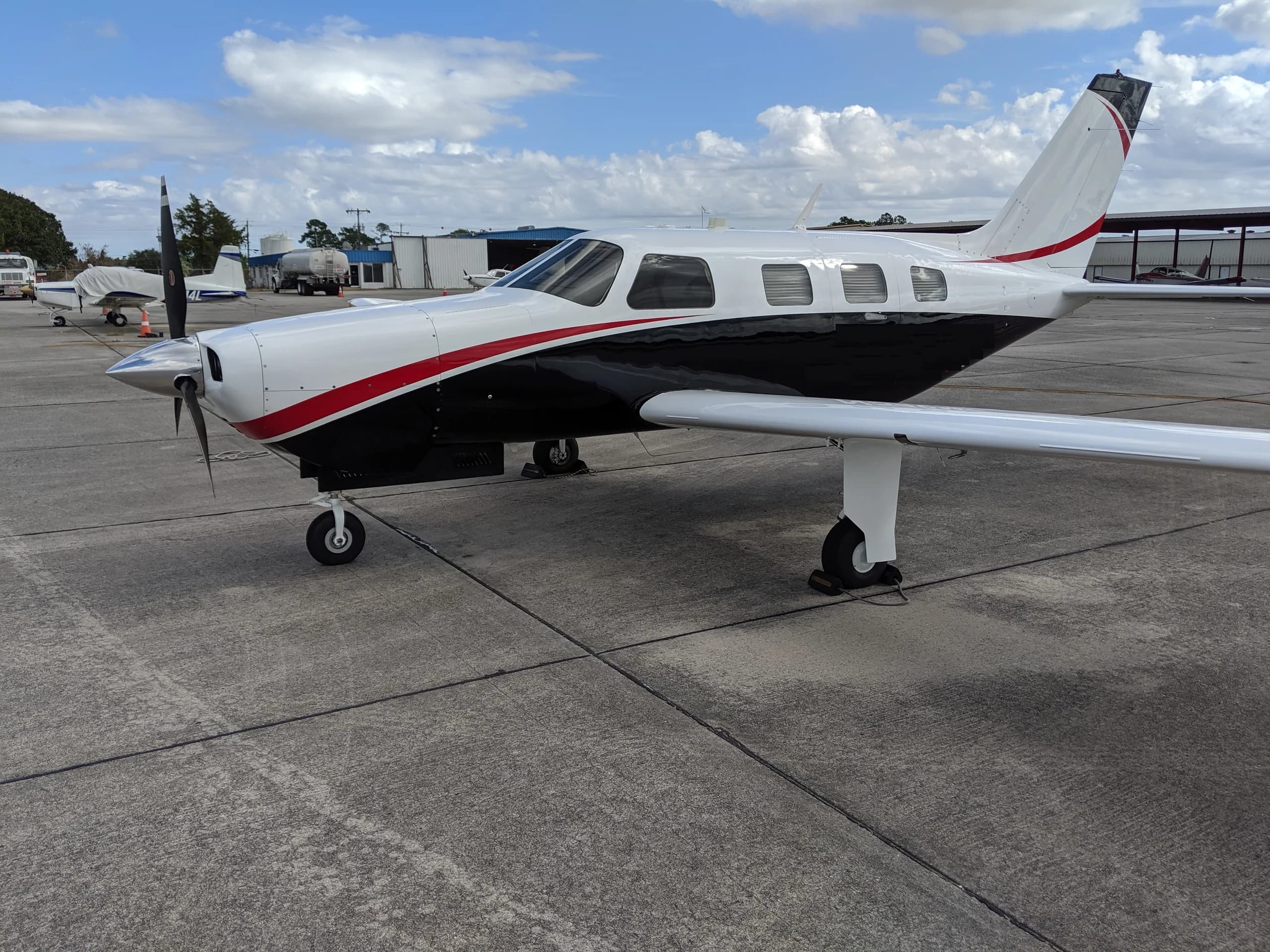 A white and black twin-engine propeller aircraft with a red stripe parked on an asphalt tarmac.