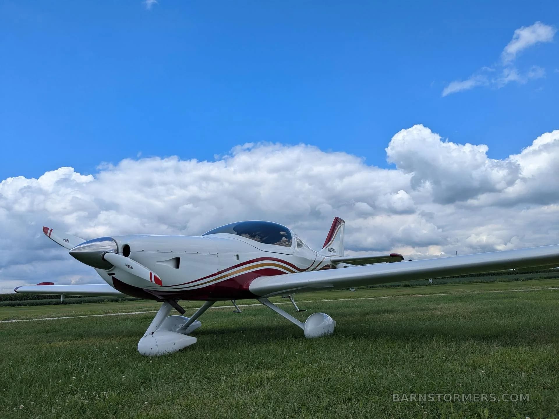 A white and red aircraft with a propeller is parked on a grassy field under a partly cloudy sky.