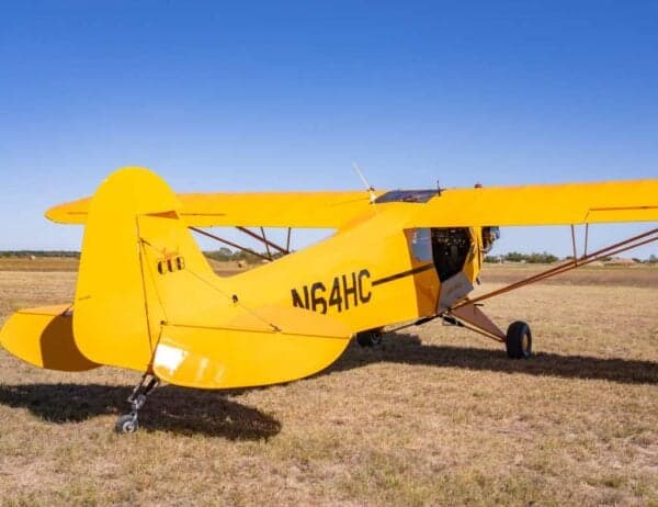A rear-side view of the yellow Legend Cub aircraft, registration N64HC, parked on a grassy field.
