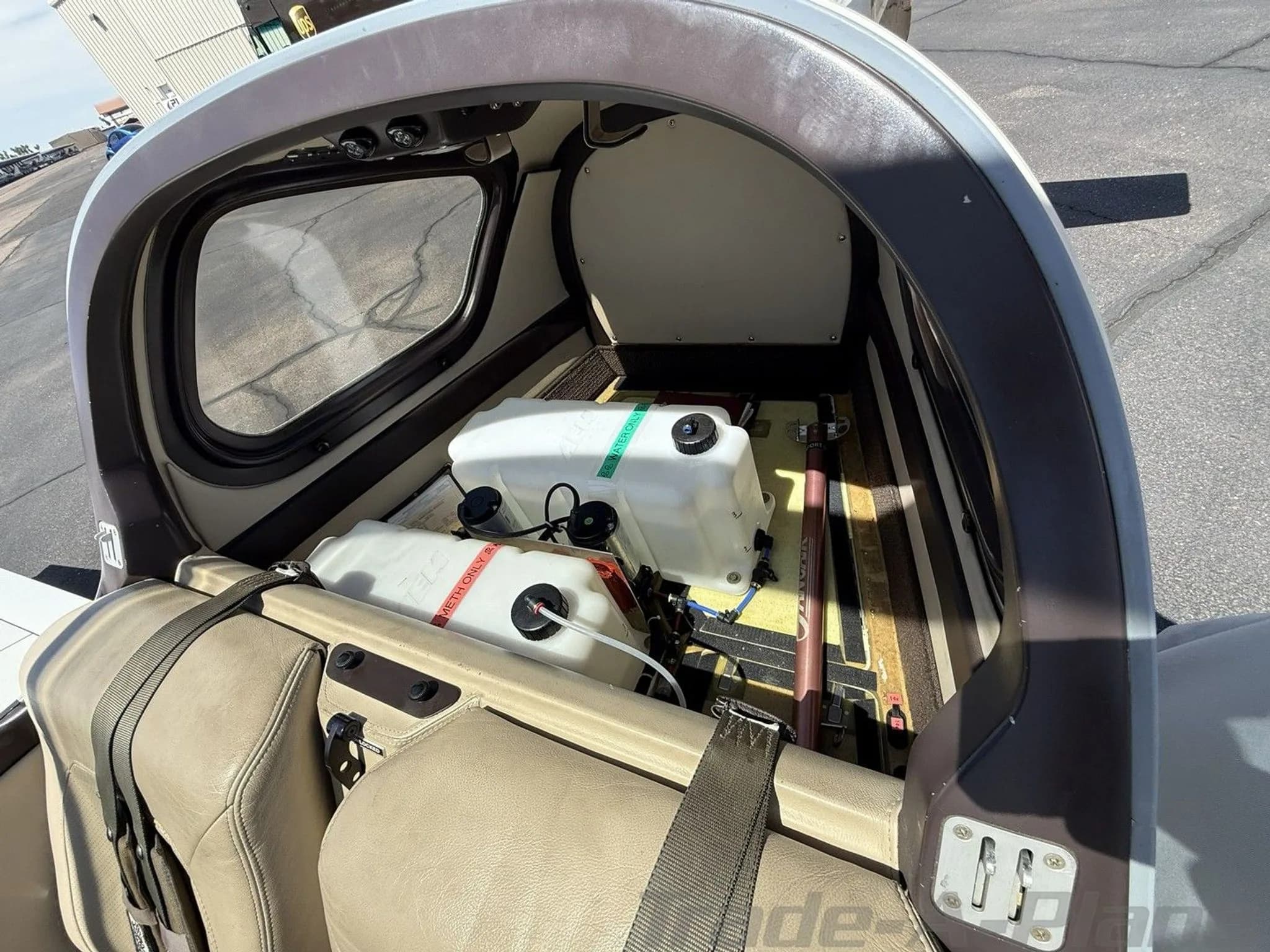 A view into the aircraft's rear compartment showing two white liquid containers and beige interior trim.