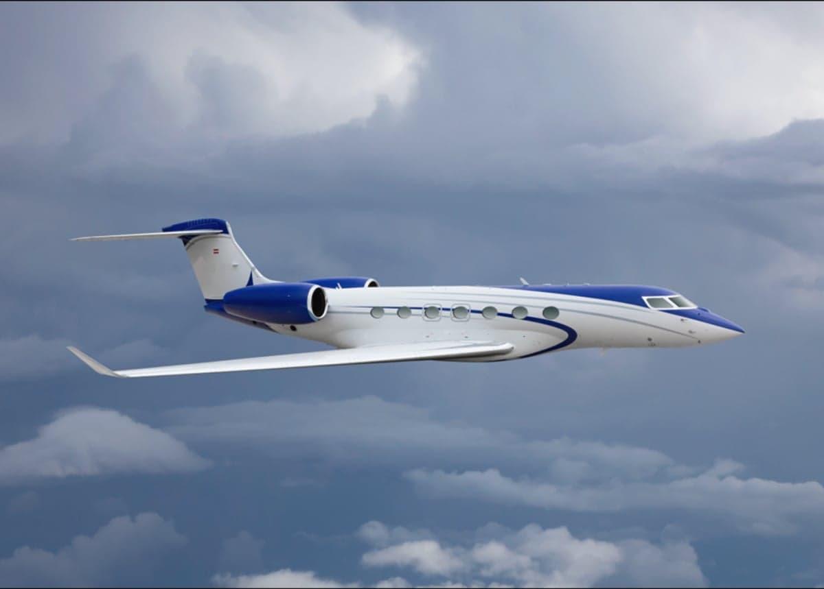 A private jet with blue and white paint scheme flying in the sky.