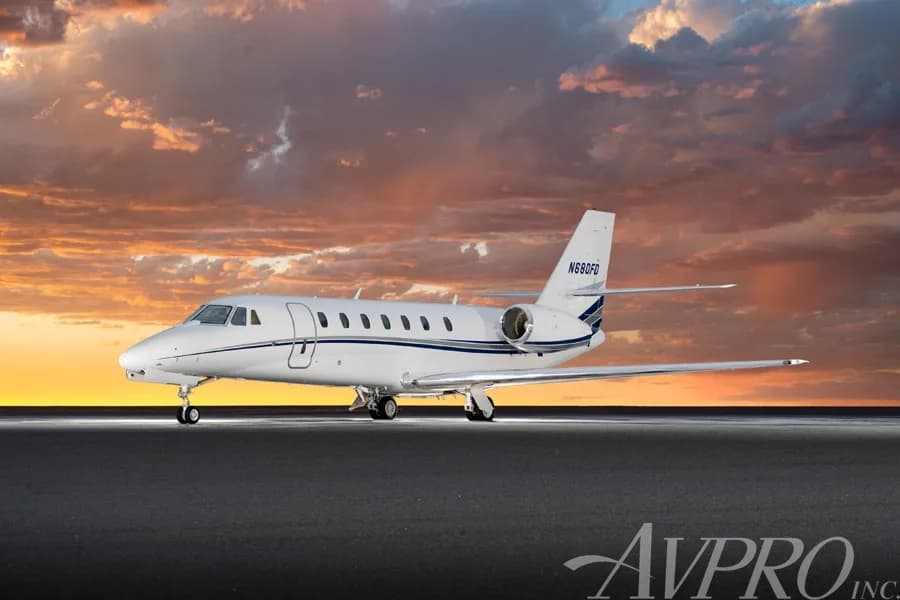 A white Cessna Citation Sovereign (N680FD) with blue and grey stripes on the fuselage, parked on a tarmac against a dramatic sunset sky.