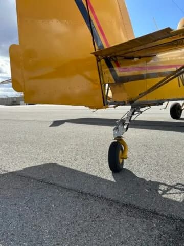 Close-up view of the tail wheel and rear fuselage of a yellow crop duster aircraft.