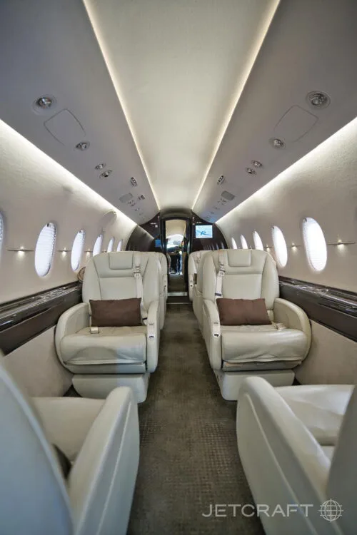 A well-lit view of the aircraft cabin with light-colored leather seats and overhead lighting strips.