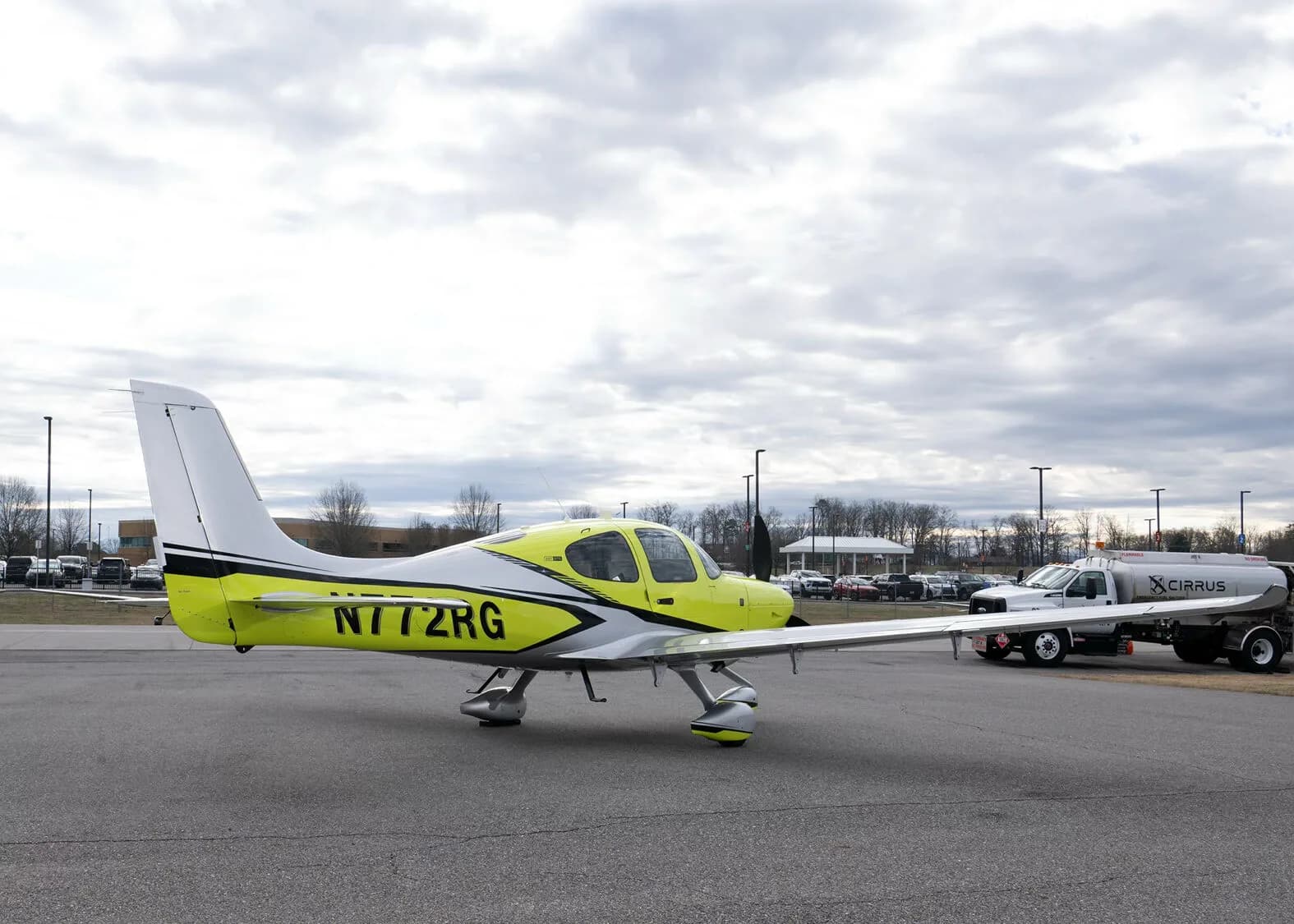 A side view of the yellow and silver Cirrus SR22, N772RG, parked on an airfield with a Cirrus fuel truck in the background.