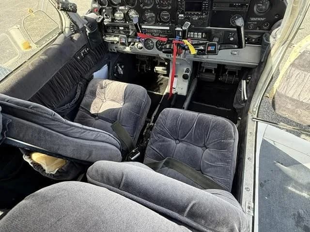 The cockpit and front cabin of the Piper Cherokee aircraft, showing grey upholstered seats and the instrument panel.