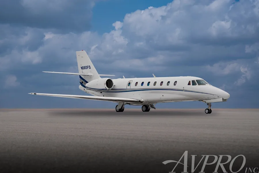 A side view of the white Cessna Citation Sovereign (N680FD) with blue and grey stripes, parked on a tarmac under a cloudy blue sky.