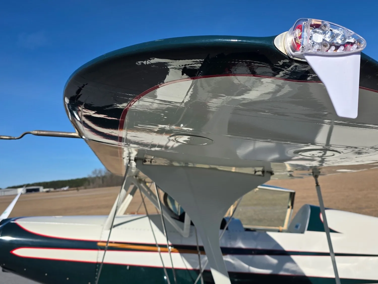 A close-up view of the upper wingtip and navigation light of the green and white biplane.