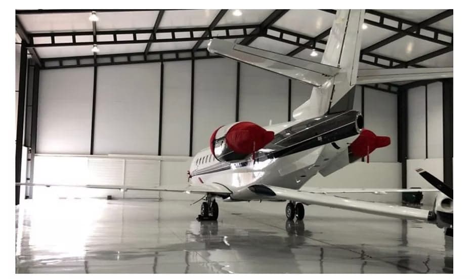 The rear of a white and black aircraft is parked inside a hangar.