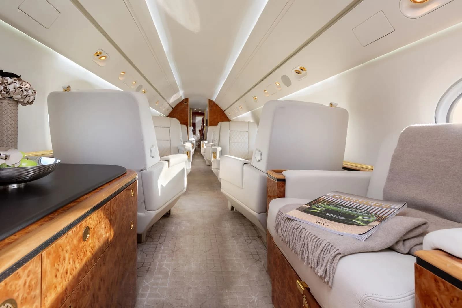 A view down the aisle of a luxurious aircraft cabin with white leather seats and wood accents.