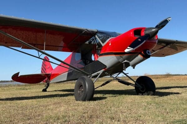 A red and gray Legend Cub aircraft is parked on a grassy field.