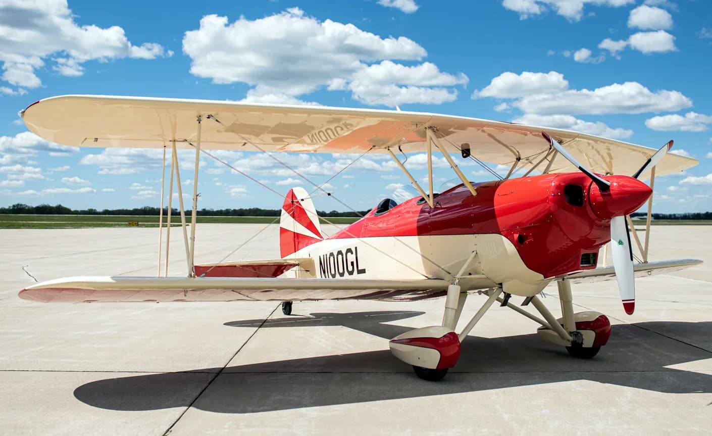 A red and white biplane with tail number N100GL is parked on the tarmac.