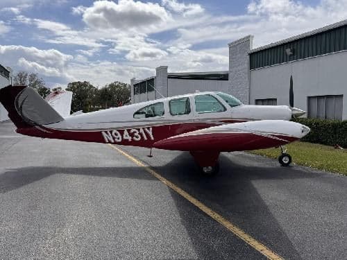 A Beechcraft Bonanza with a red and white paint scheme is parked on the tarmac.