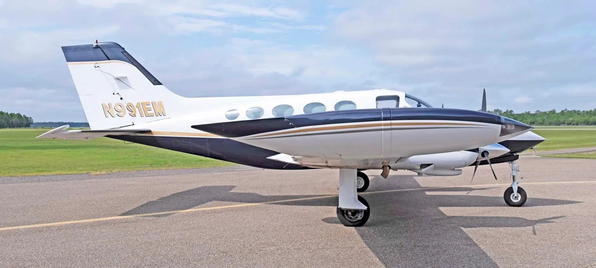 A side view of the white and dark blue Cessna 414 Chancellor, registration N991EM, parked on an airfield.