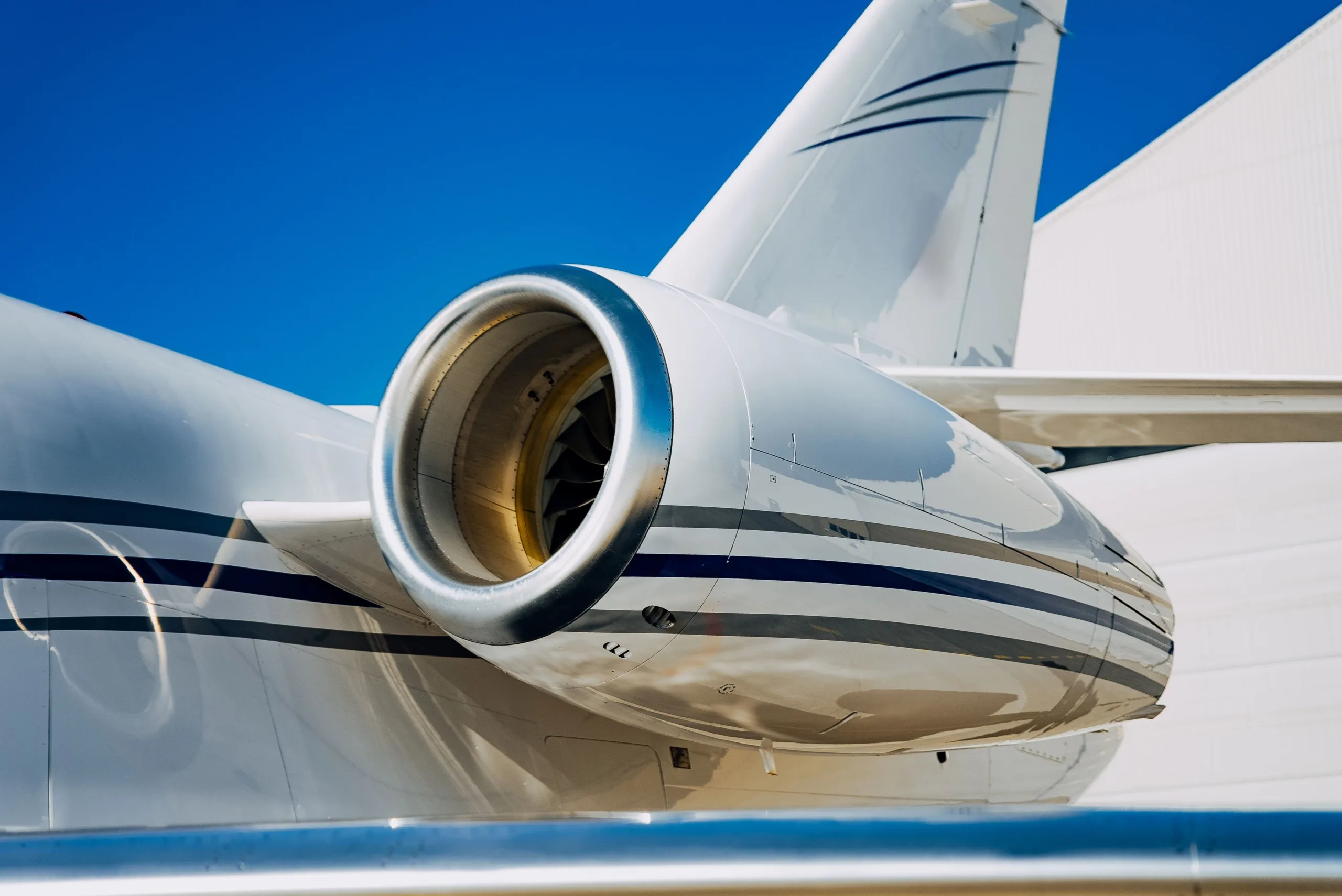 A close-up view of the rear engine and tail section of a white business jet with blue and grey stripes.