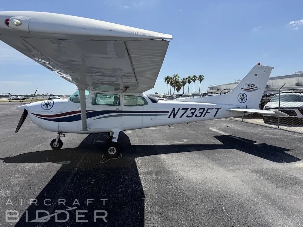 A side view of the white Cessna Skyhawk N733FT with blue and red stripes parked on an asphalt ramp.