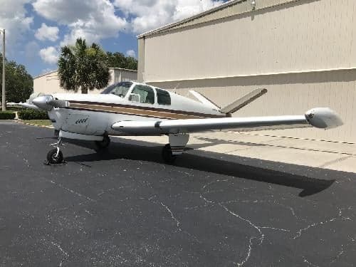 A Beechcraft Bonanza sits on the tarmac in front of a building.
