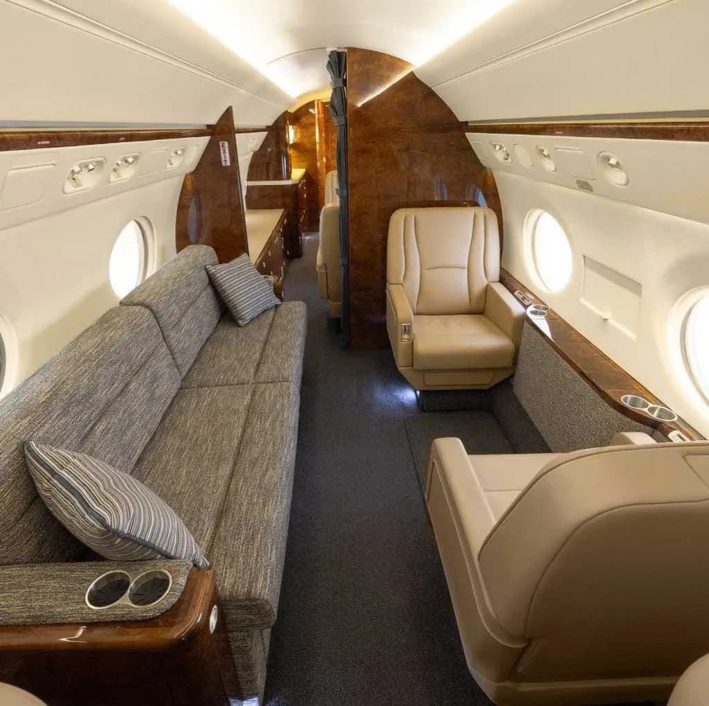 A view of the business jet's cabin interior showing a long sofa and individual tan leather seats.