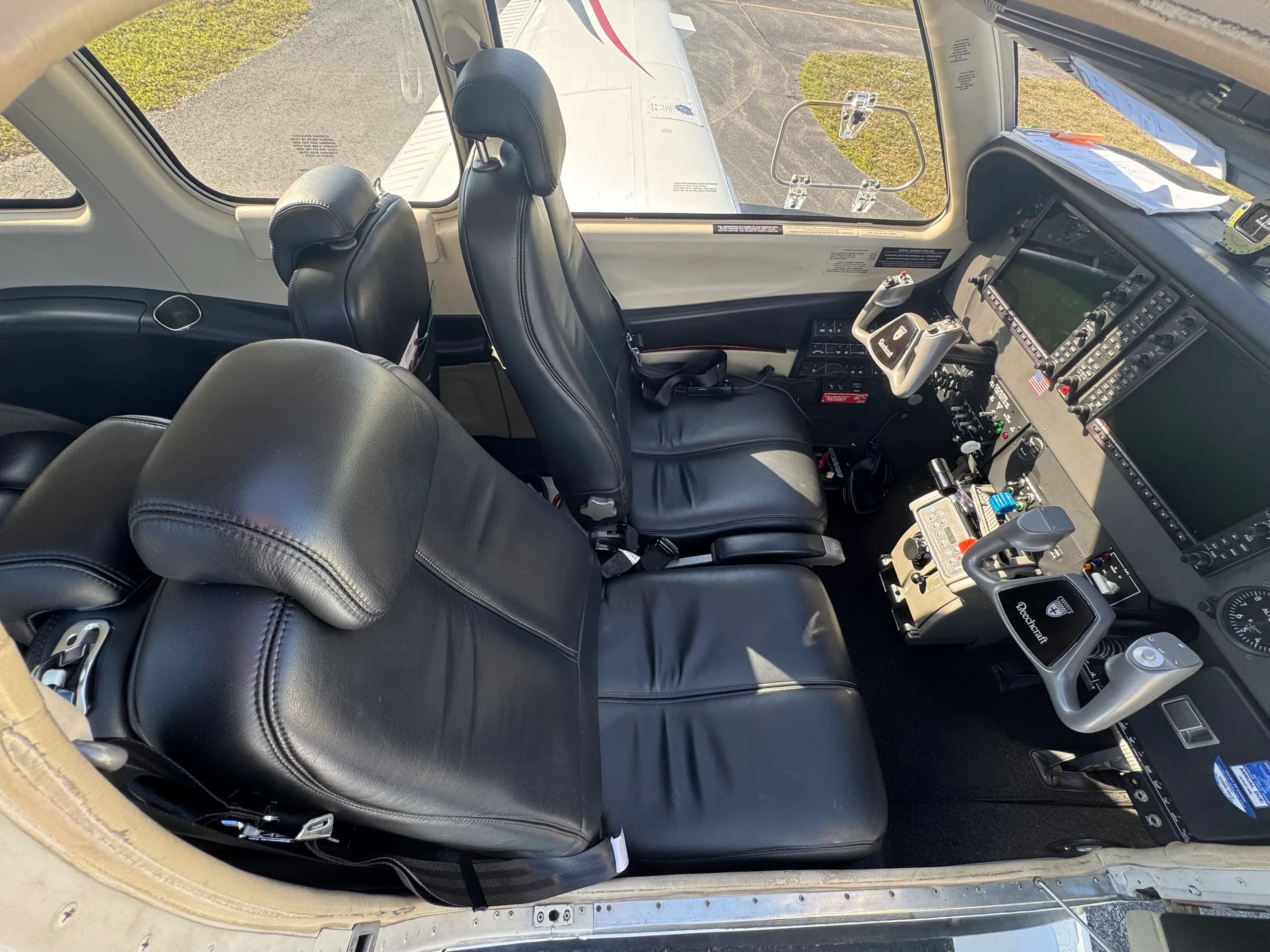 The cockpit and front two black leather seats of a Beechcraft Bonanza, showing the instrument panel and yokes.