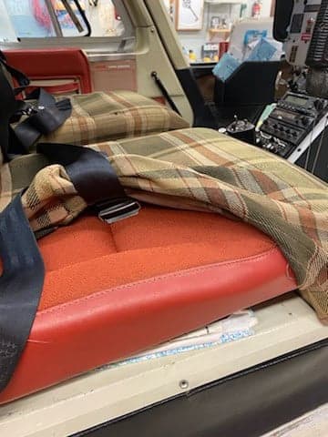 Close up of the interior of a Bell 206L-4 LongRanger helicopter with red seats and plaid seat covers.