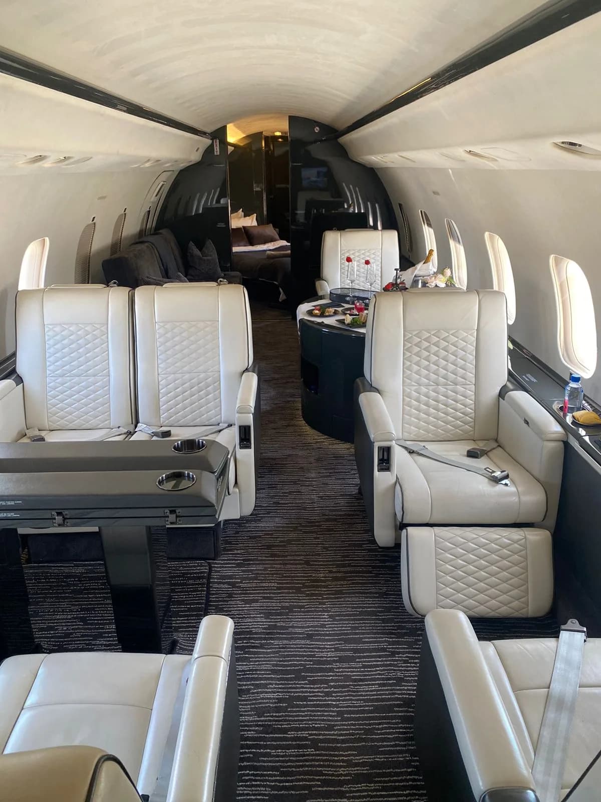 The spacious interior of a private jet featuring white quilted leather seats, a dining area, and a rear lounge.