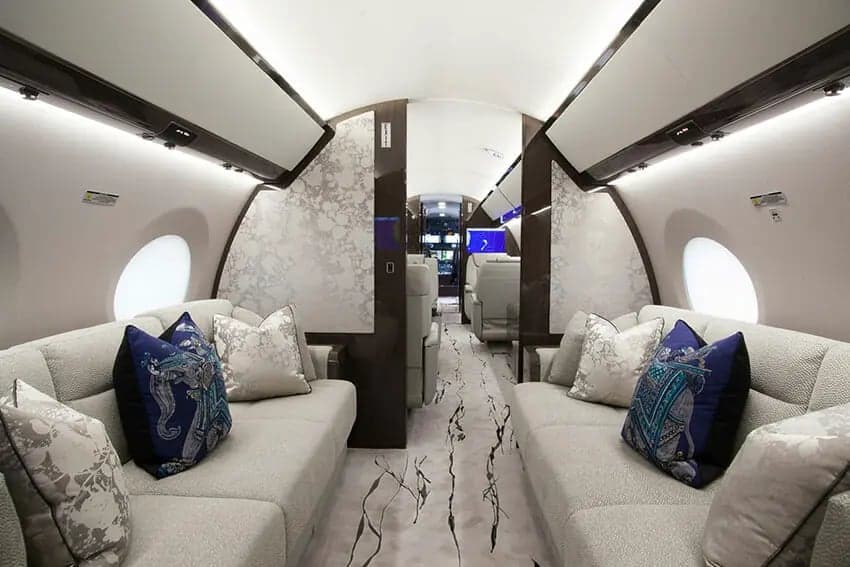 The interior of a private jet with couches and decorative pillows.