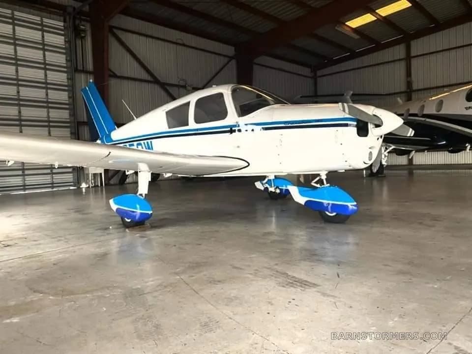 A white and blue light aircraft with blue wheel fairings parked inside a hangar.