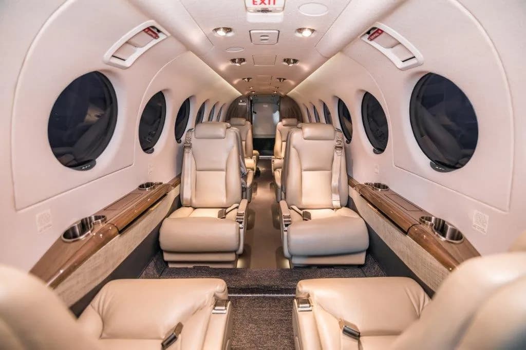 The luxurious interior cabin of a private jet with light brown leather seats and large oval windows.