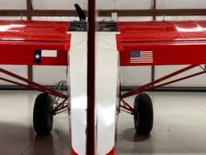 Rear view of a red and white Cubcrafters FX-3 aircraft inside a hangar, showing the tail and landing gear.