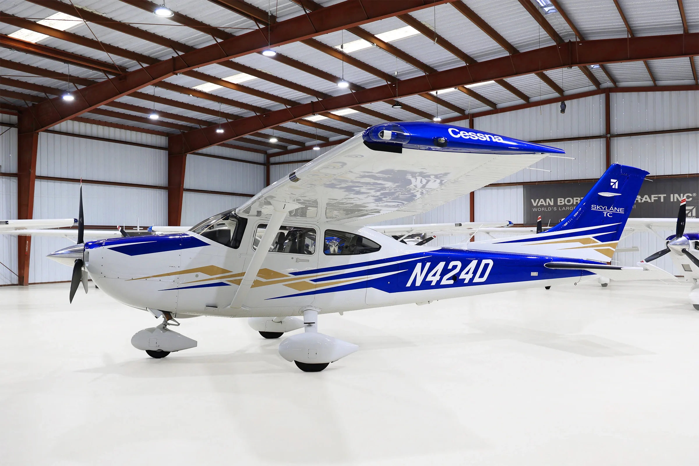 A side view of the white and blue Cessna Skylane N424D with gold accents, parked in a hangar.