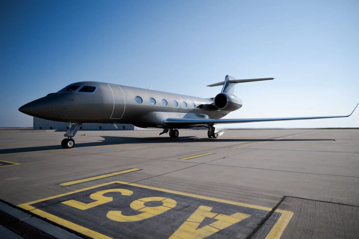 A gray Gulfstream jet is parked on the tarmac under a clear blue sky.