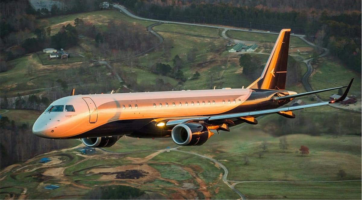 An Embraer Lineage 1000E flying over a rural landscape.