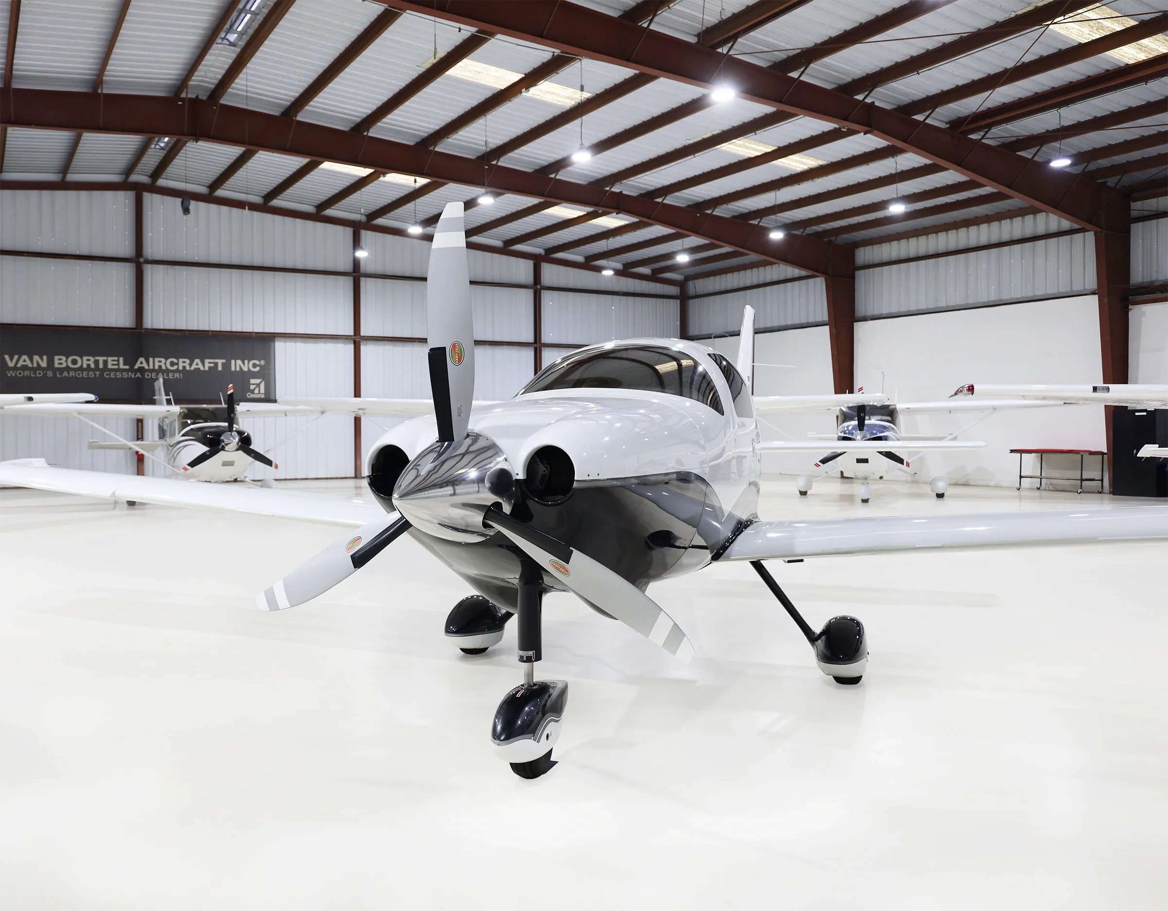 A white and black Cessna TTx aircraft (N212CJ) is parked in a hangar, viewed from the front.